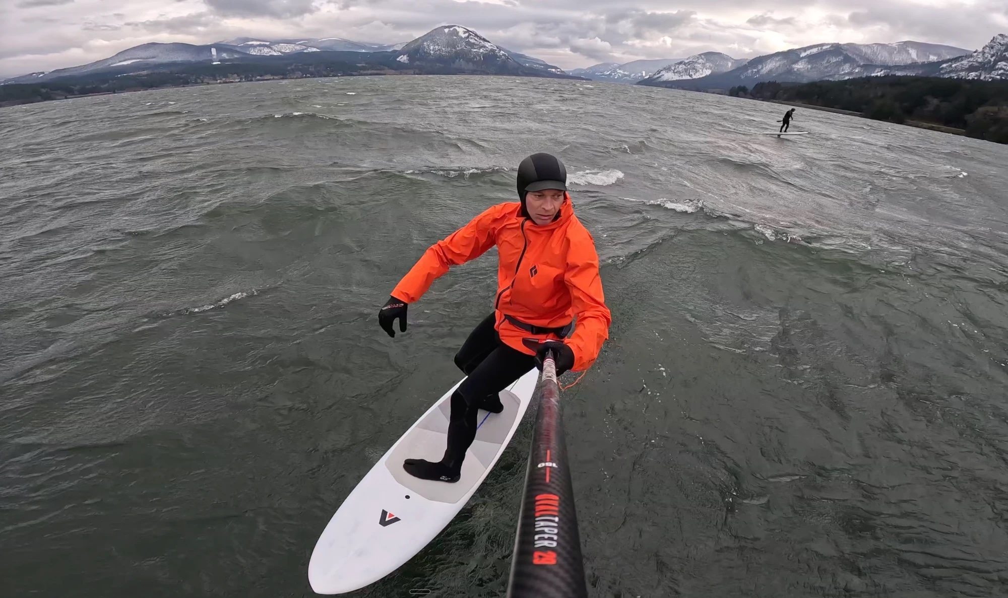 tj-winter-orange-windbreaker-sup-foil-gorge SUP foiler in a bright orange waterproof windbreaker over a hooded wetsuit on a winter day in the Columbia River Gorge